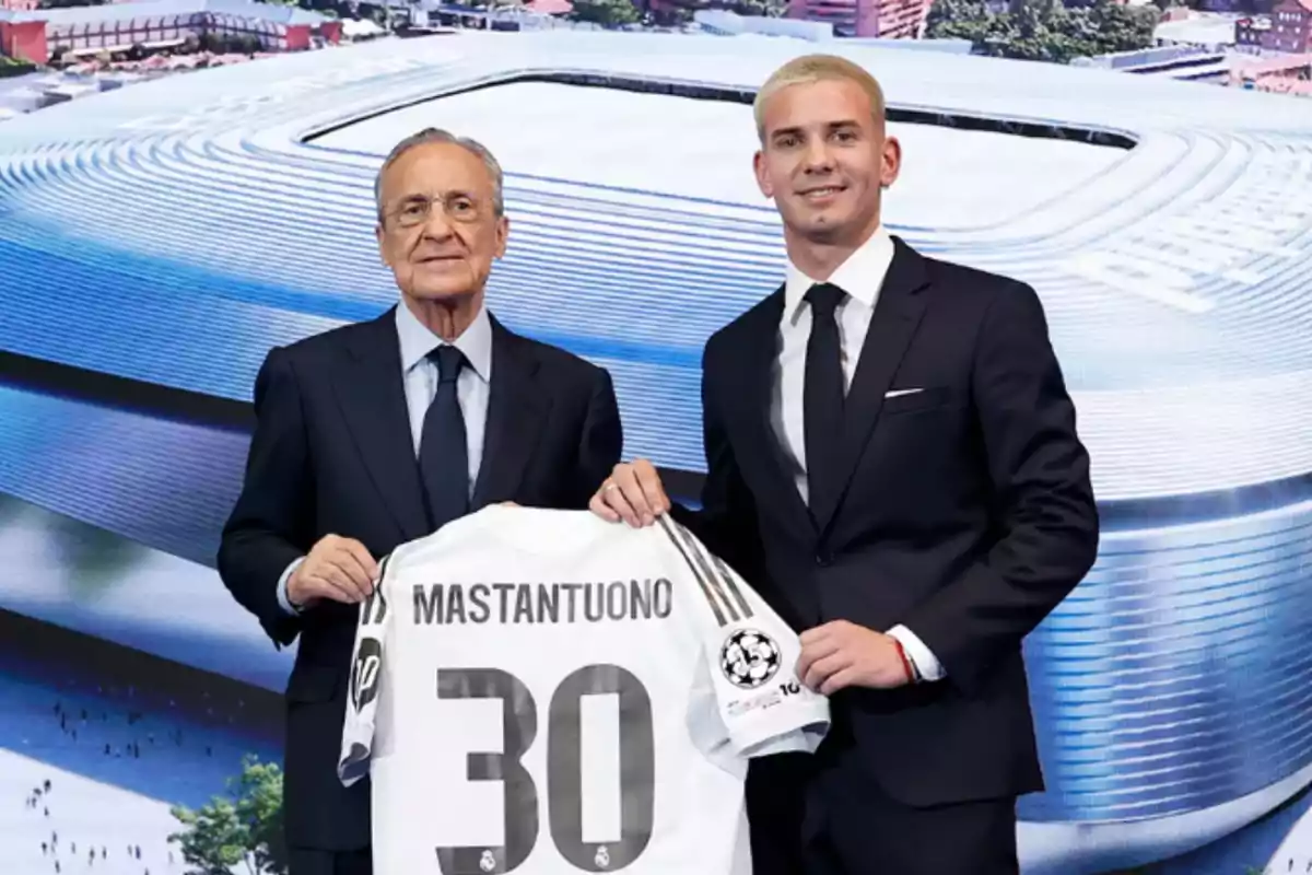 Two men in suits pose smiling, holding a soccer jersey with the name Mastantuono and the number 30 in front of an image of a modern stadium. Two men in suits pose smiling, holding a soccer jersey with the name Mastantuono and the number 30 in front of an image of a modern stadium.