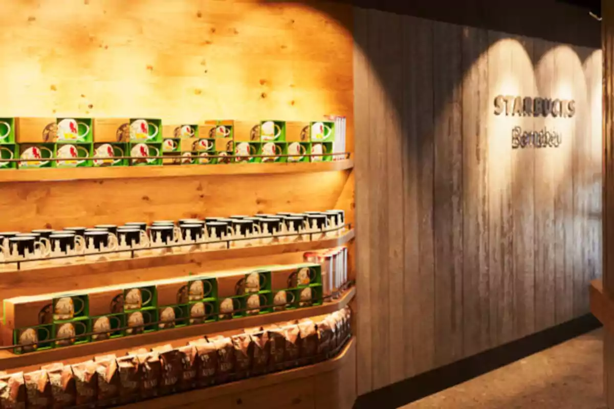 Wooden shelf with cups and Starbucks products next to a wall with the Starbucks Bernabéu sign Wooden shelf with cups and Starbucks products next to a wall with the Starbucks Bernabéu sign