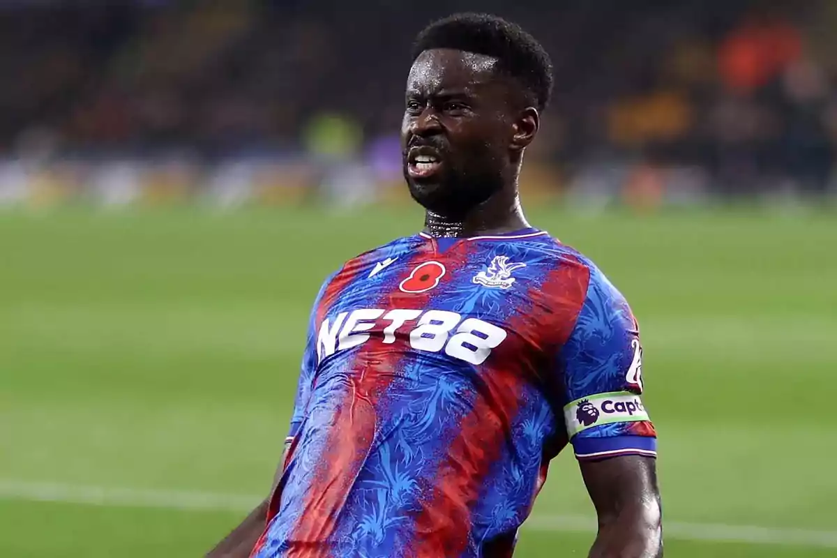 Futbolista con gesto de esfuerzo usando el uniforme azul y rojo del Crystal Palace en un partido Futbolista con gesto de esfuerzo usando el uniforme azul y rojo del Crystal Palace en un partido