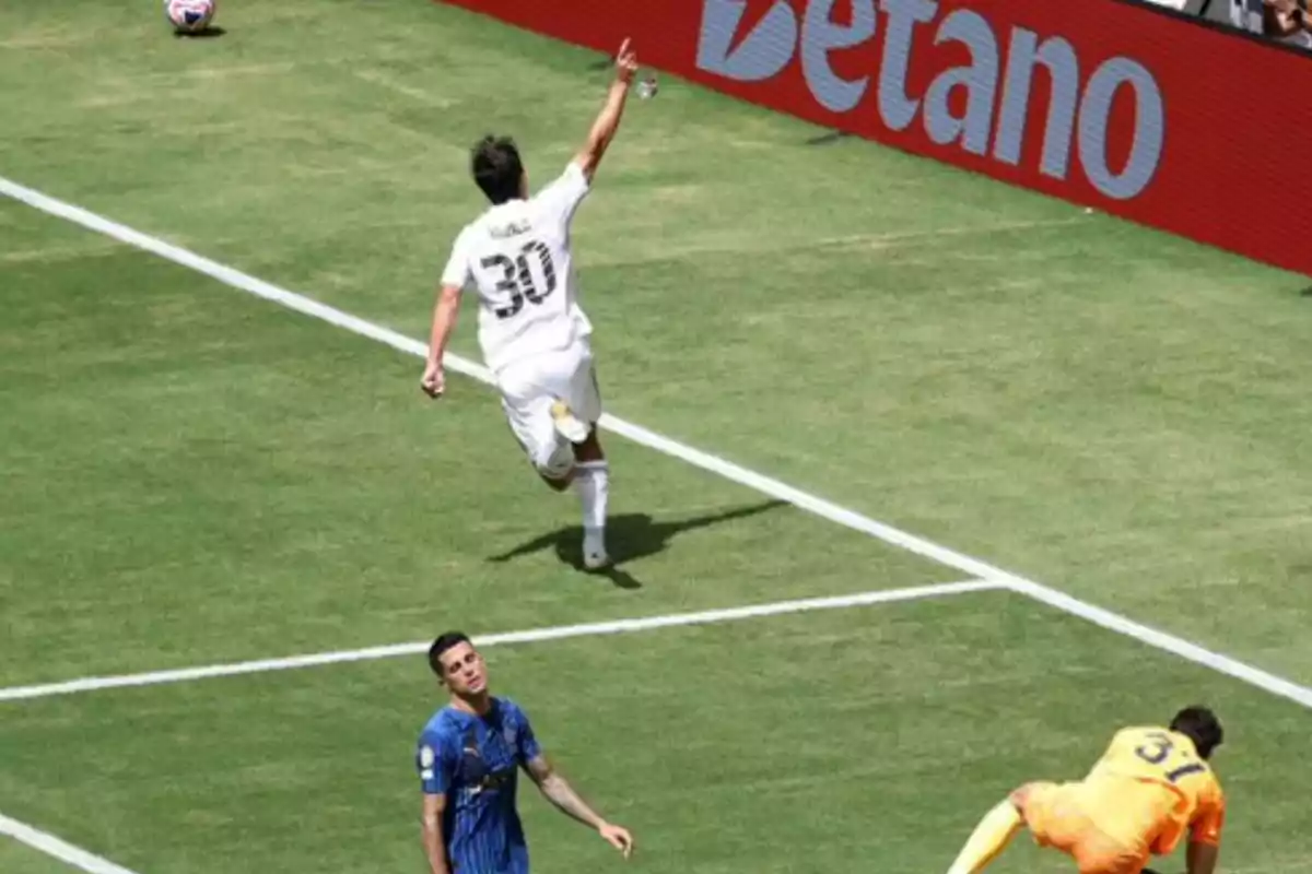 Soccer player in a white uniform celebrating a goal while a goalkeeper and a defender in blue uniforms show frustration in the box. Soccer player in a white uniform celebrating a goal while a goalkeeper and a defender in blue uniforms show frustration in the box.