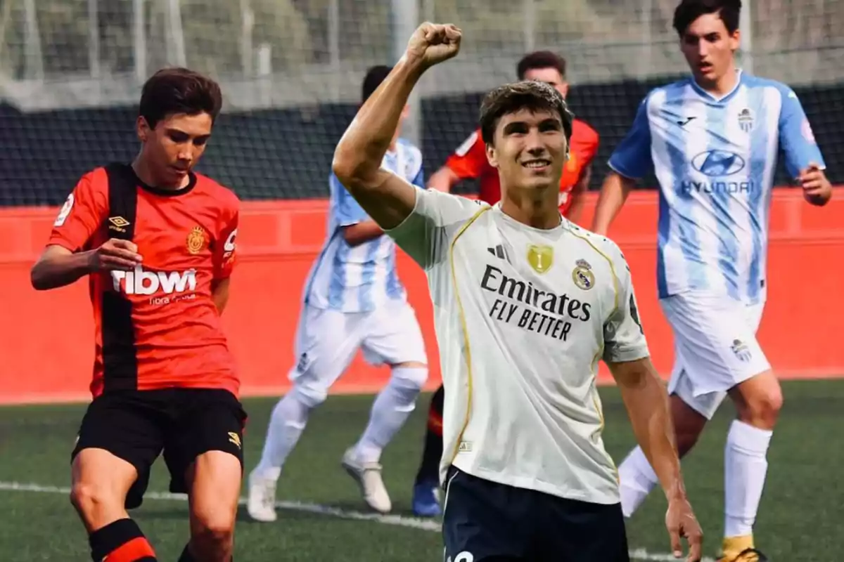 A player wearing a Real Madrid uniform celebrates by raising his fist while, in the background, a match is taking place between players in red and black uniforms and others in light blue and white on a soccer field.
