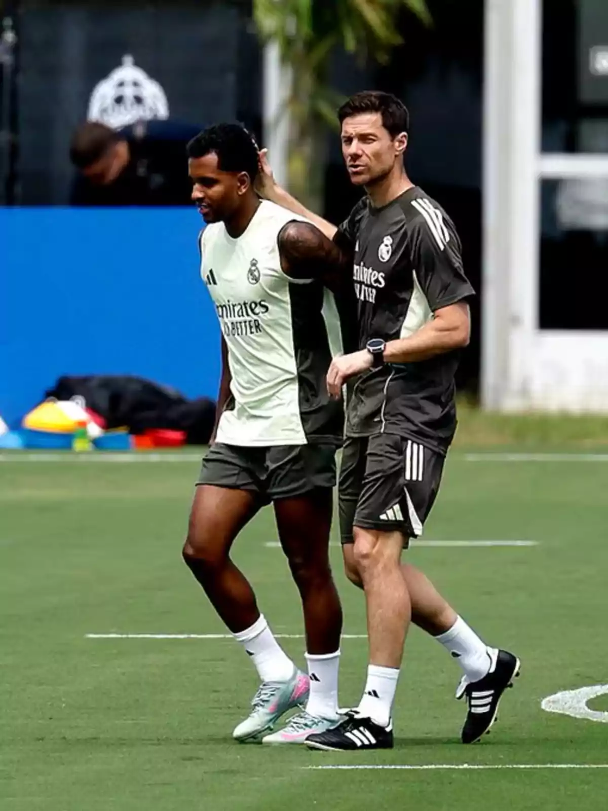 Two people wearing Real Madrid sportswear walk together on a soccer field during a training session. Two people wearing Real Madrid sportswear walk together on a soccer field during a training session.
