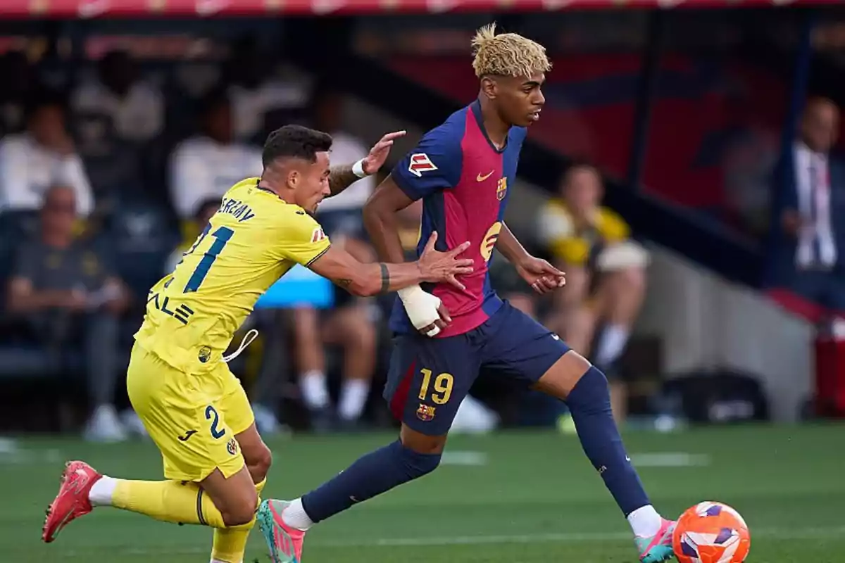 Dos futbolistas disputan el balón durante un partido uno con uniforme amarillo y el otro con uniforme azul y rojo Dos futbolistas disputan el balón durante un partido uno con uniforme amarillo y el otro con uniforme azul y rojo
