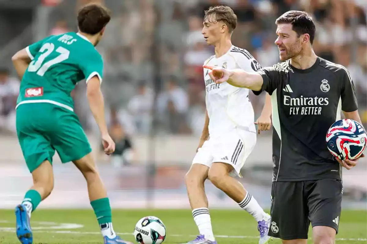 Entrenador de fútbol con uniforme negro de Real Madrid da indicaciones mientras sostiene un balón y dos jugadores disputan el balón en el campo