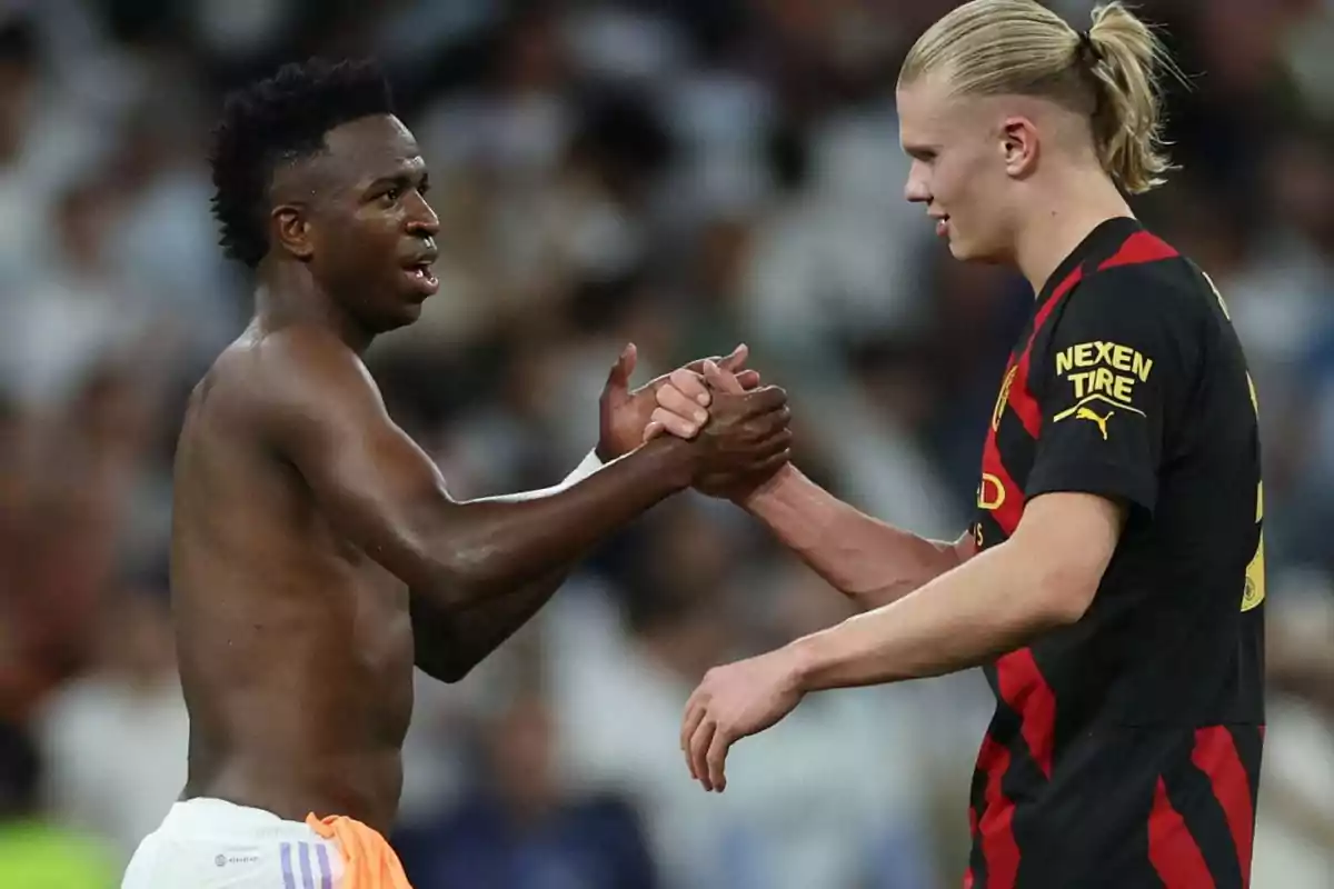 Two players greet each other on the field at the end of a match, one of them jerseyless and the other wearing a black and red uniform. Two players greet each other on the field at the end of a match, one of them jerseyless and the other wearing a black and red uniform.