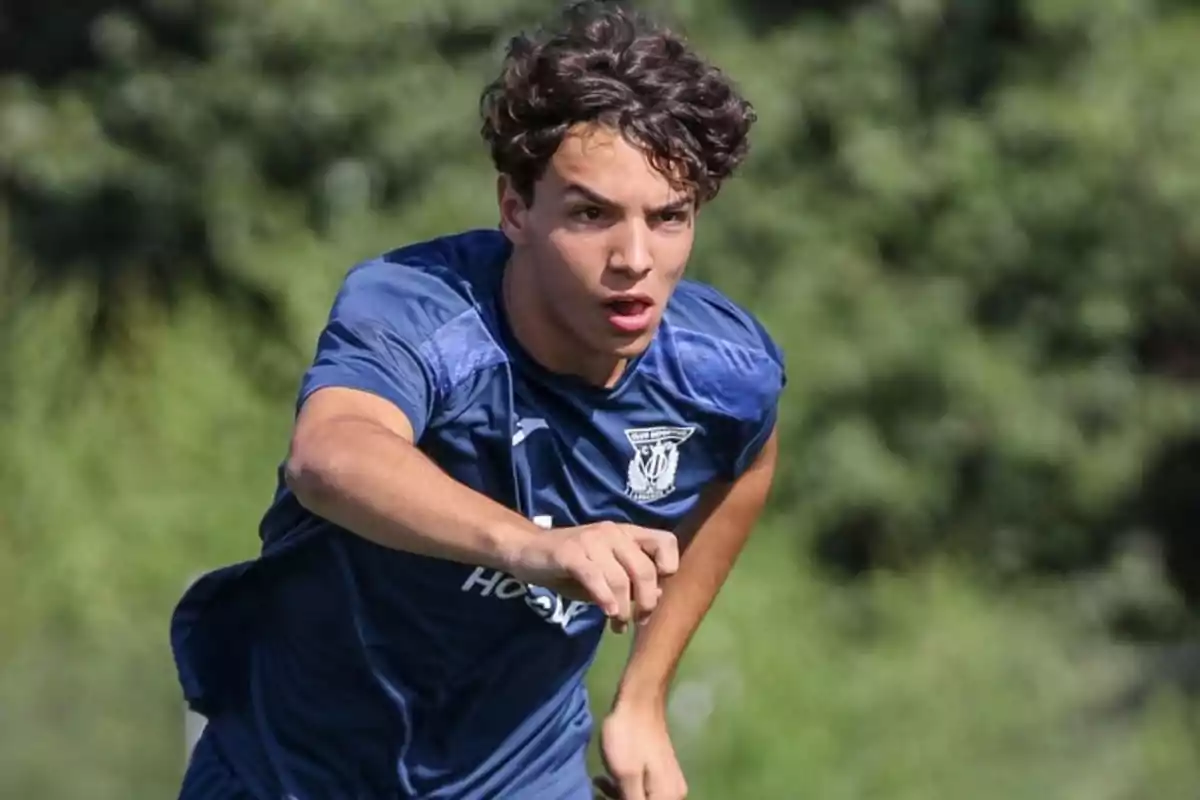 Joven futbolista corriendo en un campo de entrenamiento con camiseta azul Joven futbolista corriendo en un campo de entrenamiento con camiseta azul