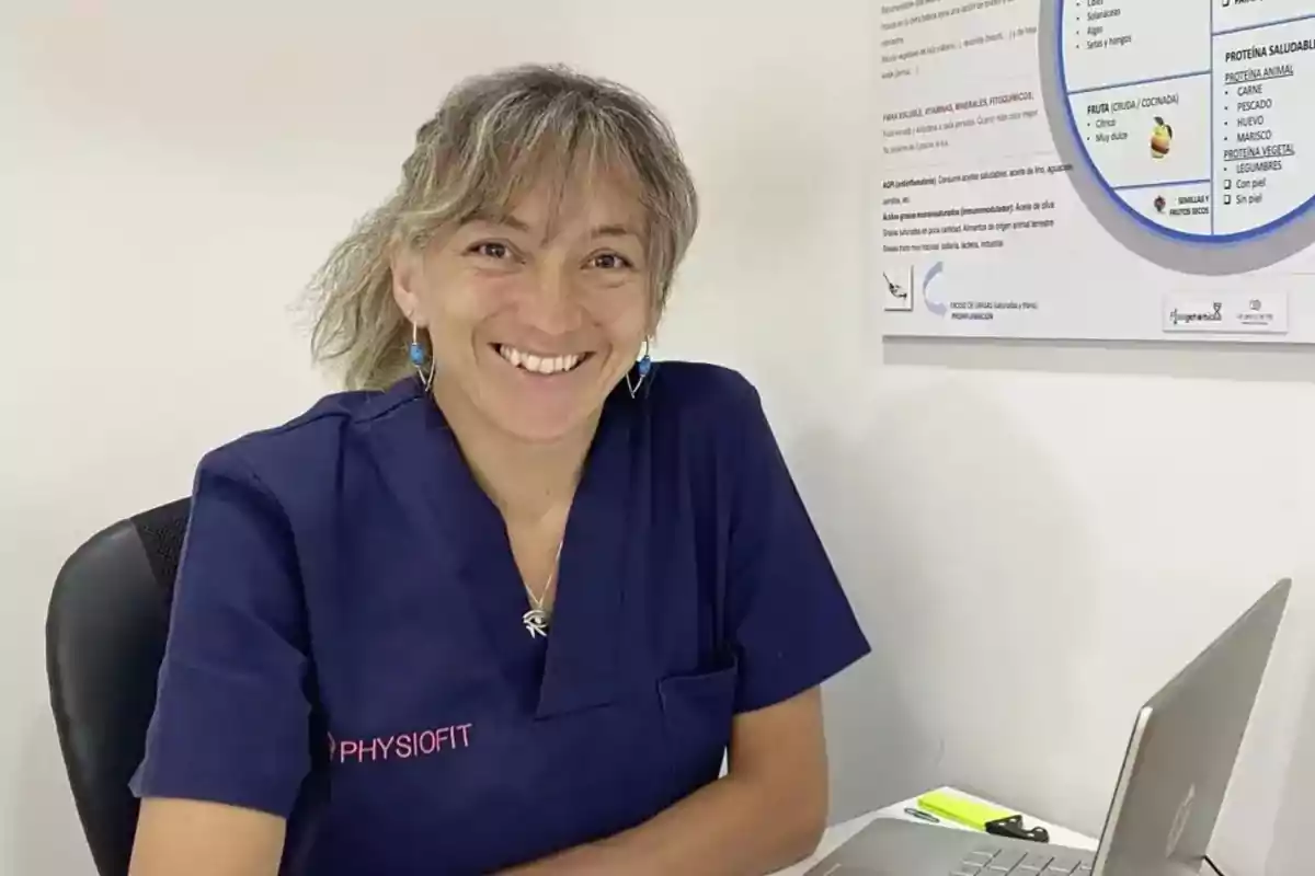Mujer con uniforme azul marino sentada en un escritorio sonriendo frente a una computadora portátil Mujer con uniforme azul marino sentada en un escritorio sonriendo frente a una computadora portátil