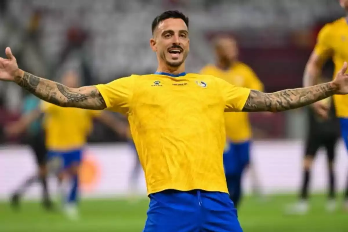 Soccer player celebrating with arms outstretched in a stadium while wearing a yellow and blue uniform