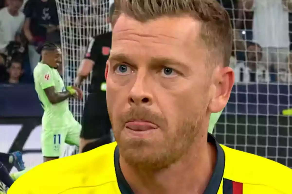Árbitro de fútbol con expresión seria en primer plano mientras un jugador y el público se ven desenfocados al fondo