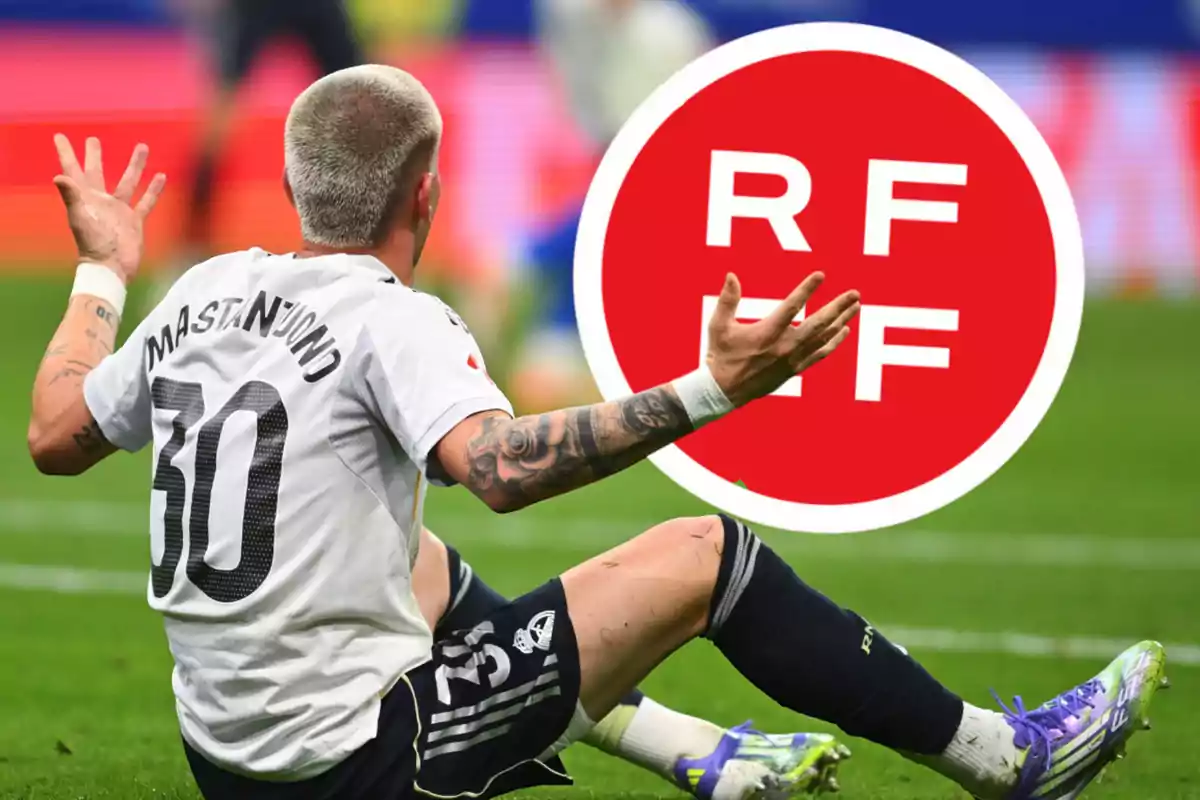 Soccer player sitting on the grass with a frustrated expression and a large RFEF logo in the background