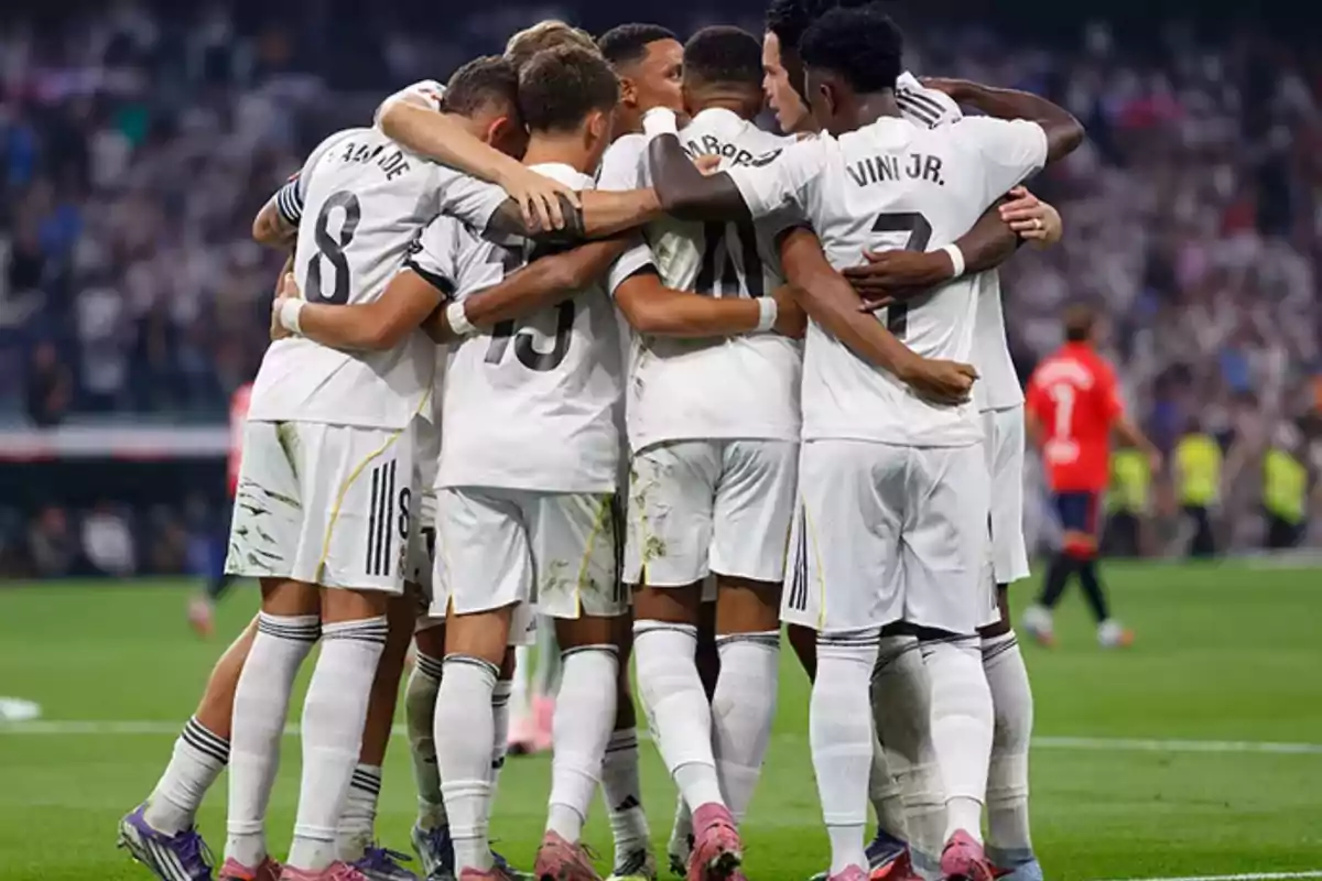 Jugadores de fútbol vestidos de blanco se abrazan en grupo celebrando en el campo durante un partido