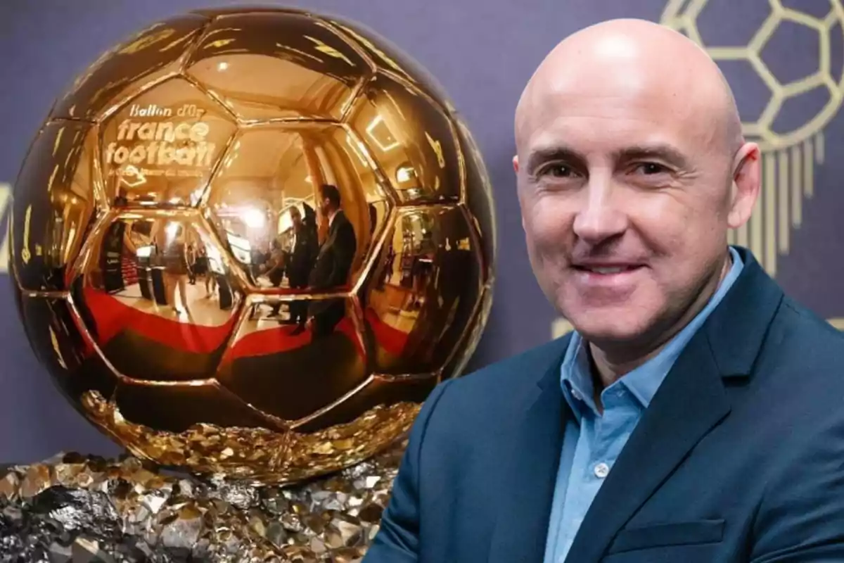 A bald man in a blue jacket smiles in front of a golden Ballon d'Or trophy.