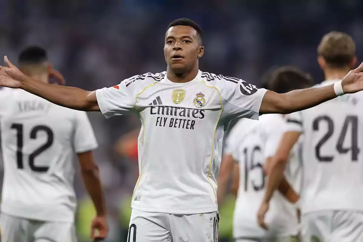 Futbolista con uniforme blanco del Real Madrid celebrando con los brazos extendidos en el campo junto a otros jugadores