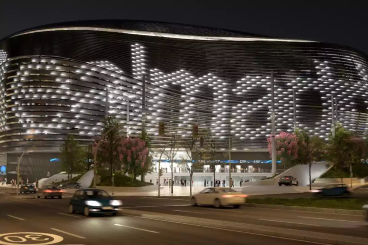 Modern stadium facade illuminated at night with cars driving by and people entering the venue Modern stadium facade illuminated at night with cars driving by and people entering the venue