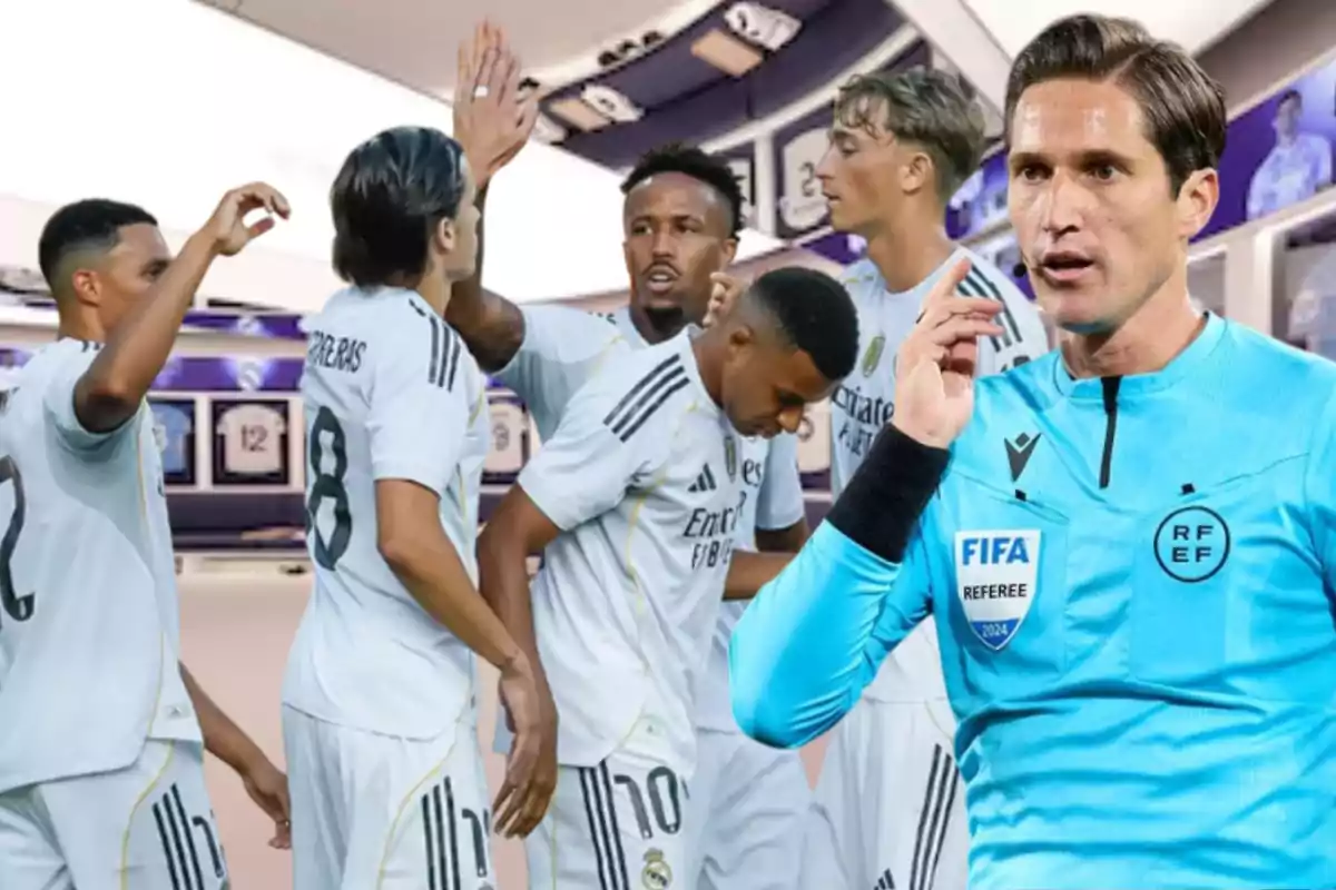 Un grupo de jugadores de fútbol con uniforme blanco celebrando mientras un árbitro con uniforme azul aparece en primer plano señalando su auricular