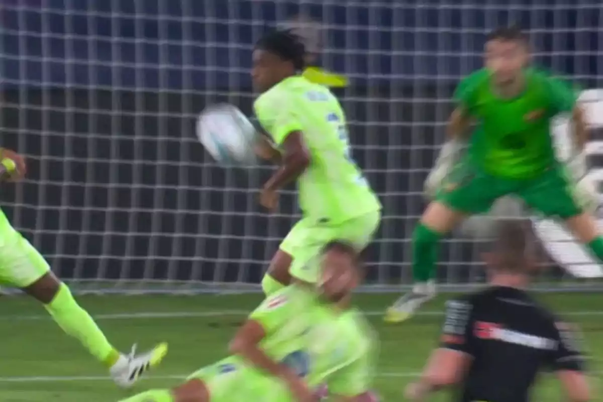 Un jugador de fútbol detiene el balón con el brazo dentro del área mientras el portero y otros jugadores observan la jugada Un jugador de fútbol detiene el balón con el brazo dentro del área mientras el portero y otros jugadores observan la jugada