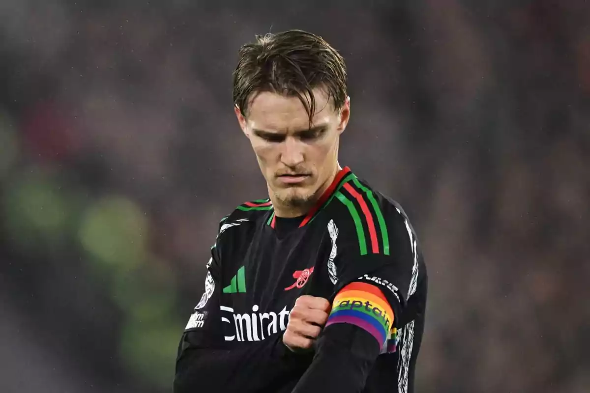 Futbolista con uniforme negro y detalles en verde y rojo ajustando un brazalete de capitán con los colores del arcoíris Futbolista con uniforme negro y detalles en verde y rojo ajustando un brazalete de capitán con los colores del arcoíris