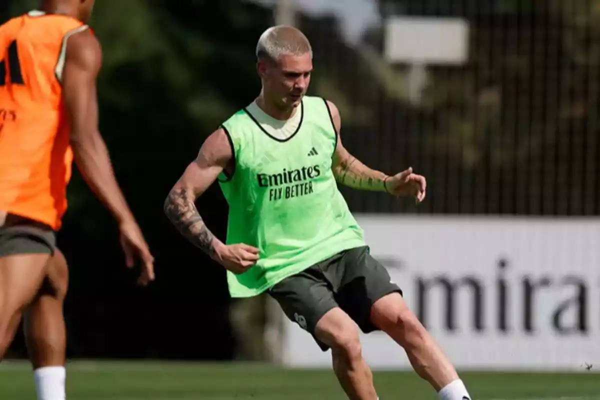 Futbolista rubio con chaleco verde entrenando en un campo de fútbol junto a otro jugador con chaleco naranja Futbolista rubio con chaleco verde entrenando en un campo de fútbol junto a otro jugador con chaleco naranja