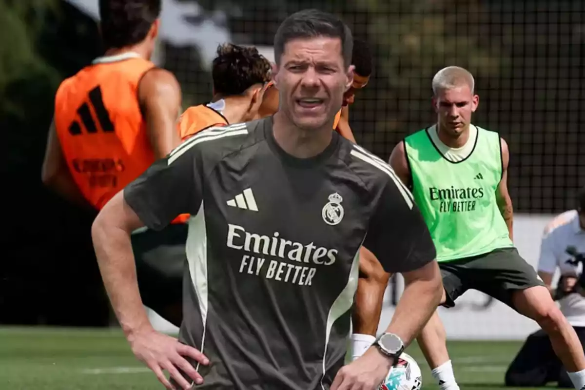 Entrenador del Real Madrid en primer plano con jugadores entrenando al fondo en un campo de fútbol