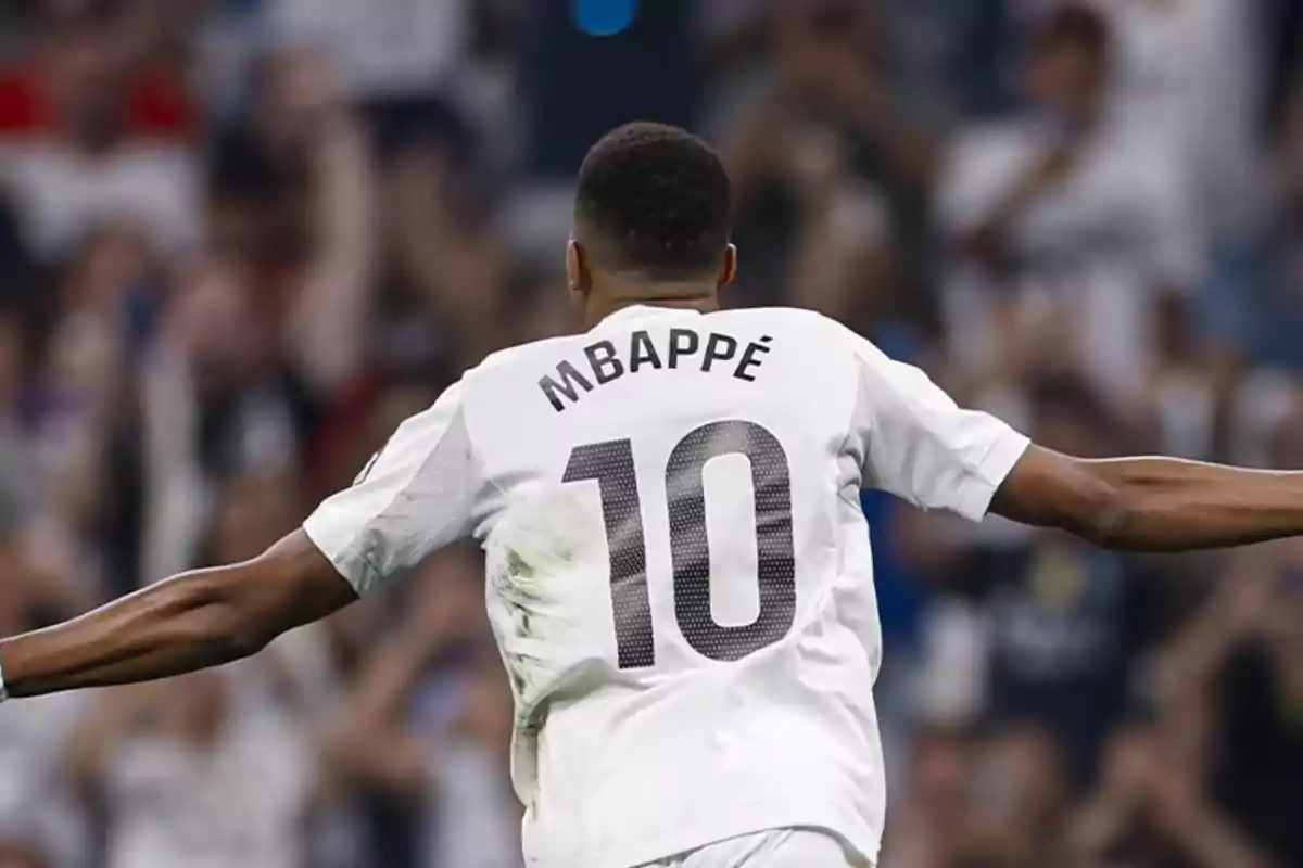 Soccer player wearing number 10 and the name Mbappé celebrating with arms outstretched in a stadium full of fans Soccer player wearing number 10 and the name Mbappé celebrating with arms outstretched in a stadium full of fans