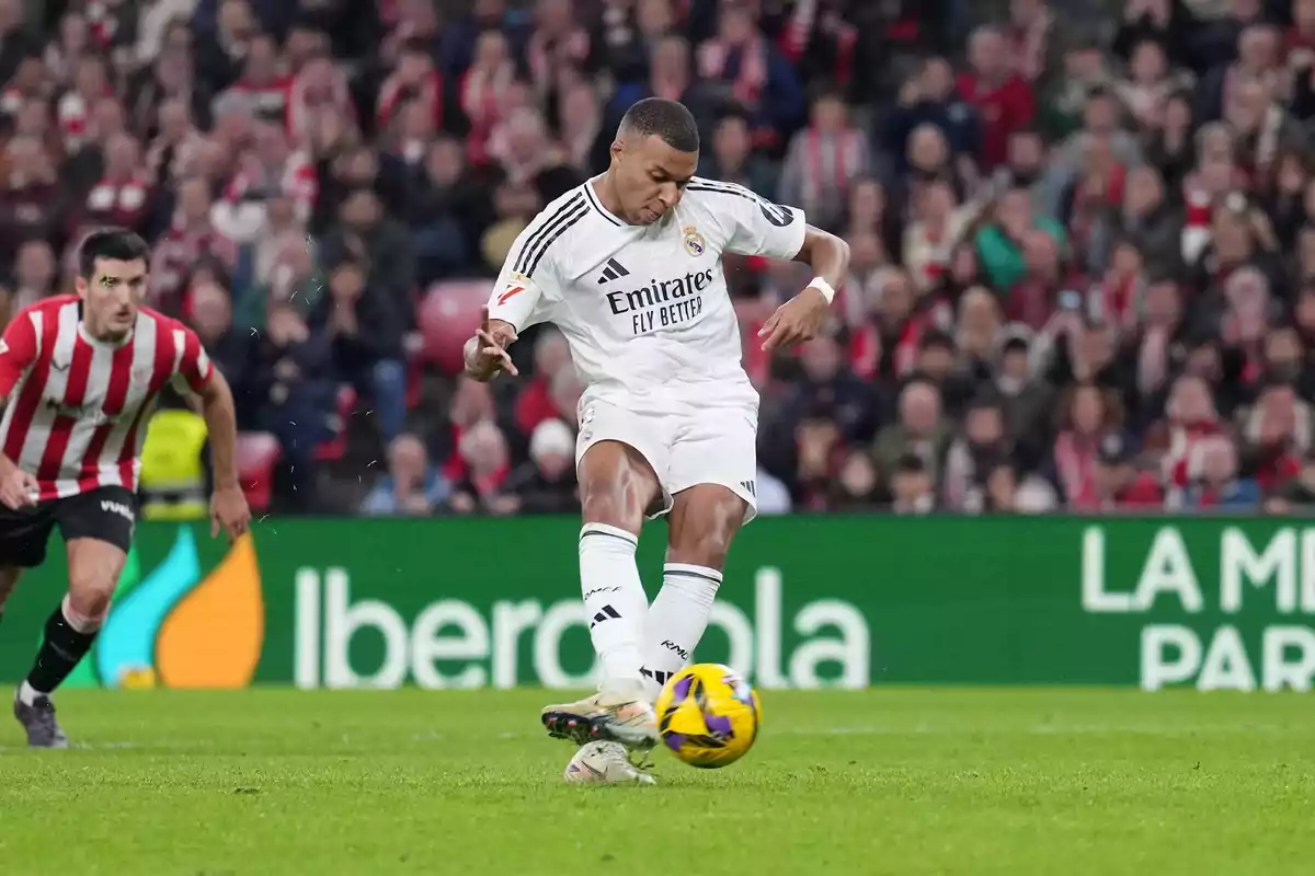 Futbolista del Real Madrid pateando el balón durante un partido contra el Athletic Club con público en las gradas de fondo Futbolista del Real Madrid pateando el balón durante un partido contra el Athletic Club con público en las gradas de fondo