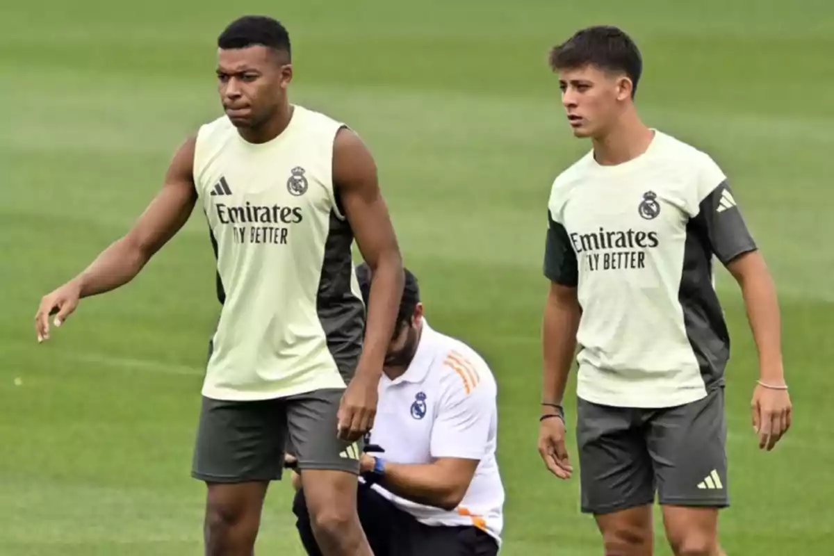 Dos futbolistas del Real Madrid entrenando en el campo con ropa de entrenamiento y un preparador físico al fondo Dos futbolistas del Real Madrid entrenando en el campo con ropa de entrenamiento y un preparador físico al fondo