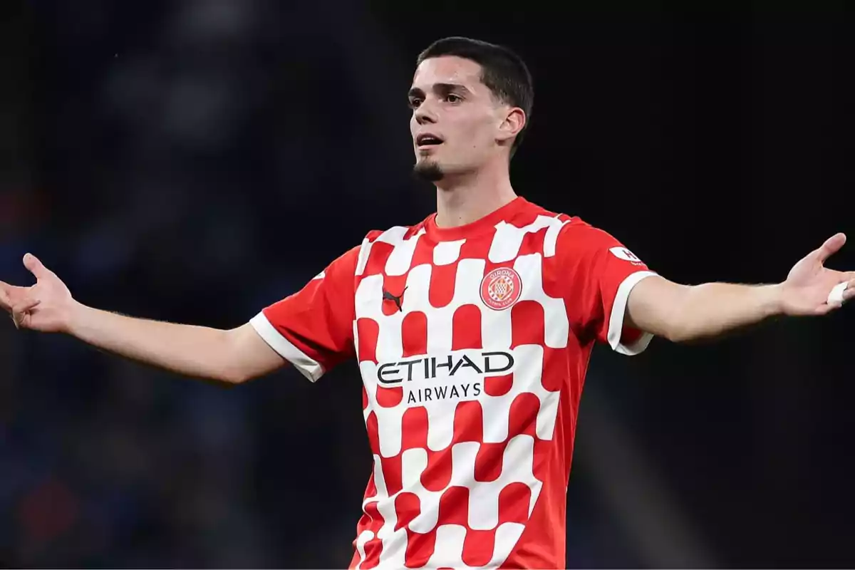 Soccer player in a red and white Girona FC uniform gesturing with open arms on the field Soccer player in a red and white Girona FC uniform gesturing with open arms on the field