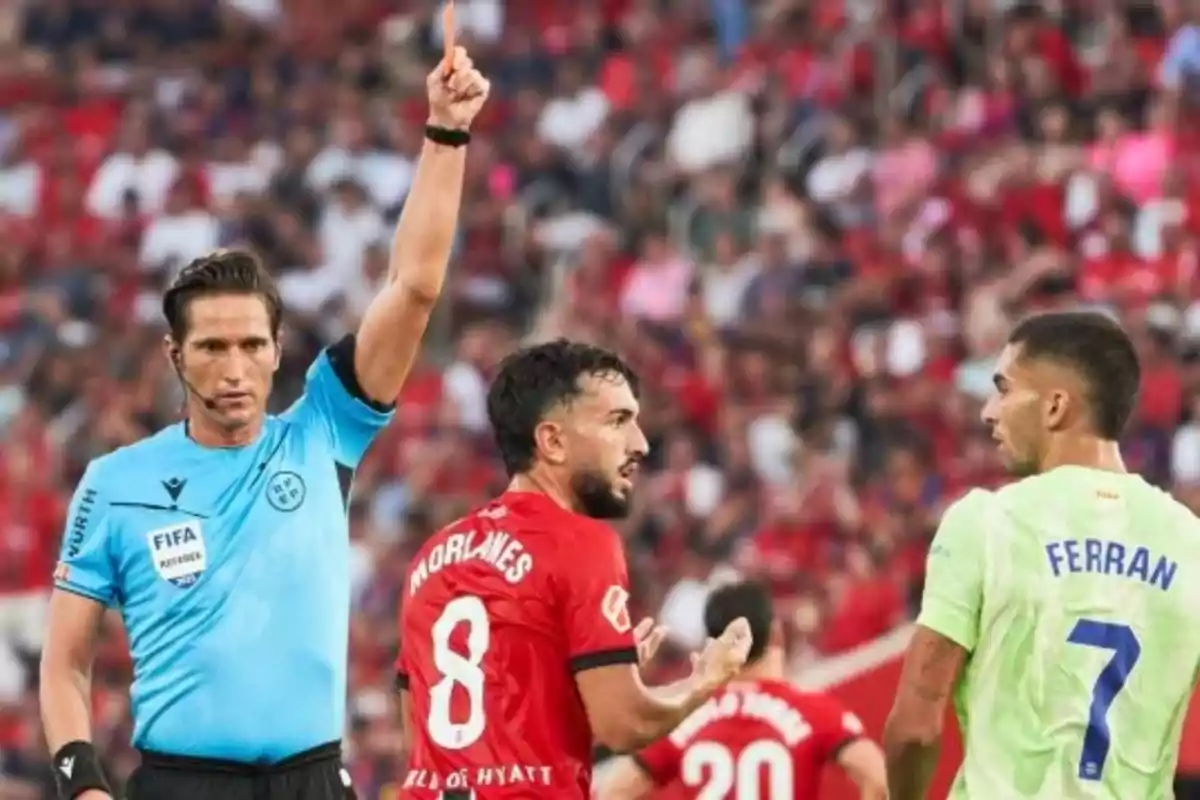 A referee shows a red card to a player during a soccer match while other players watch the scene. A referee shows a red card to a player during a soccer match while other players watch the scene.