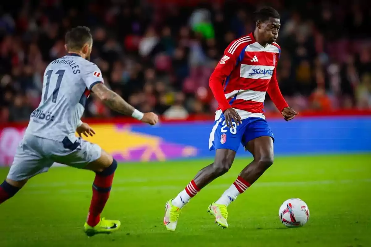 Two players compete for the ball during a match in a stadium full of spectators. Two players compete for the ball during a match in a stadium full of spectators.