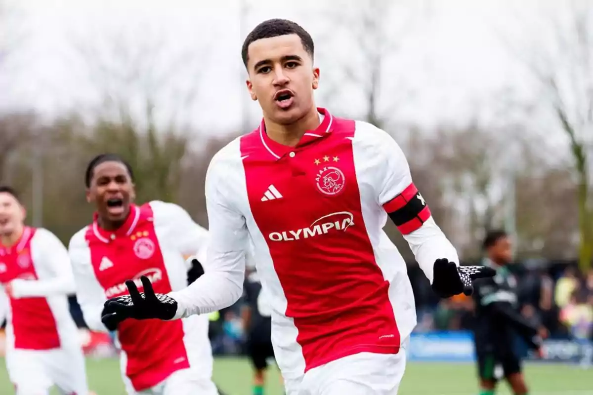 Jugador del Ajax celebrando un gol en el campo con compañeros al fondo Jugador del Ajax celebrando un gol en el campo con compañeros al fondo