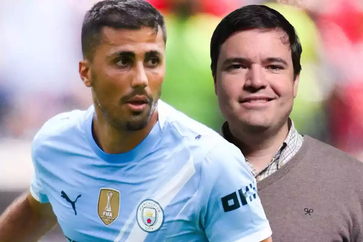 Un futbolista con uniforme del Manchester City está en primer plano mientras un hombre con suéter marrón y camisa clara aparece al fondo con un fondo desenfocado.