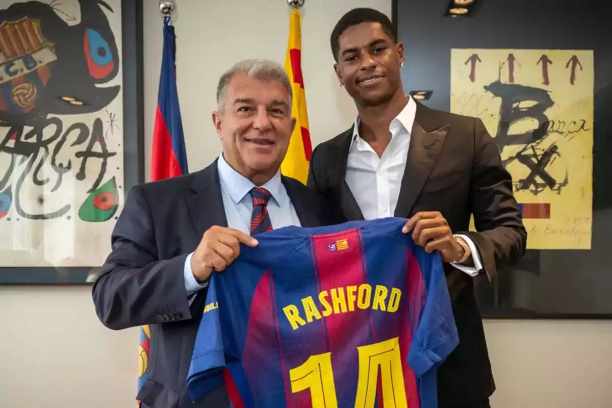 Dos personas sonríen mientras sostienen una camiseta del FC Barcelona con el nombre Rashford y el número 10 en una oficina decorada con banderas y cuadros del club.