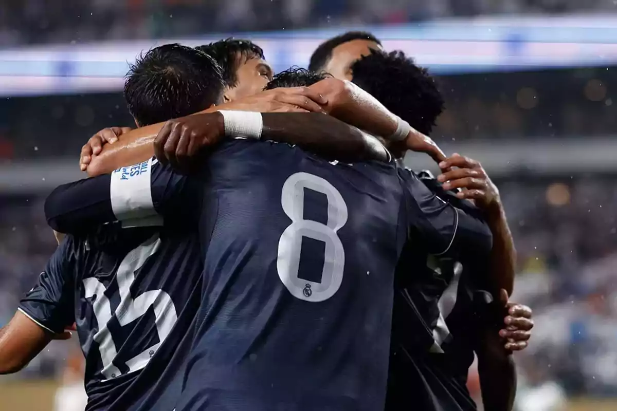 Soccer players in dark blue uniforms celebrate by hugging on the field during a match.