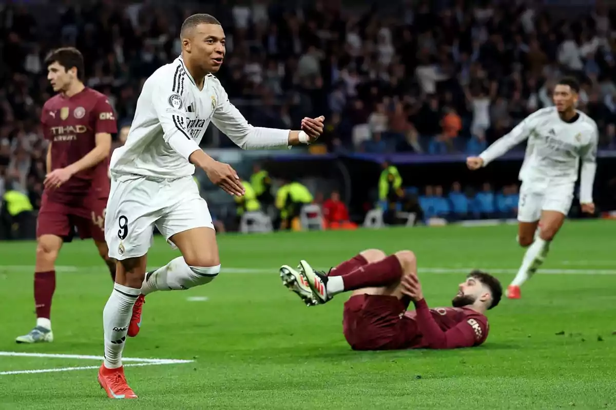 A player in a white uniform celebrates a goal while an opposing player in a burgundy uniform is on the ground and other players watch the play in a stadium full of spectators. A player in a white uniform celebrates a goal while an opposing player in a burgundy uniform is on the ground and other players watch the play in a stadium full of spectators.