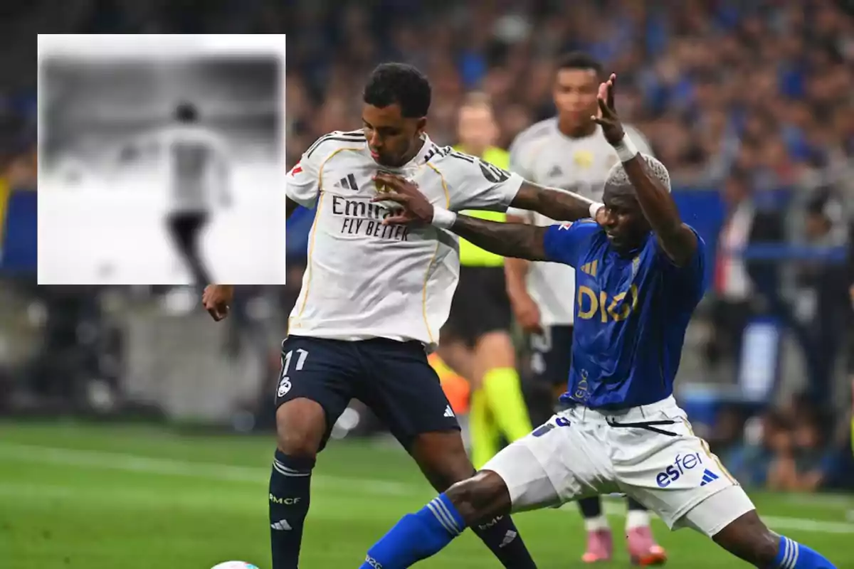 Dos futbolistas disputan el balón durante un partido mientras al fondo se observa una imagen borrosa de otro jugador