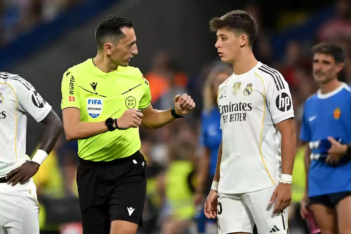 A soccer referee talks with a Real Madrid player during a match; both appear focused on the situation in the game. A soccer referee talks with a Real Madrid player during a match; both appear focused on the situation in the game.