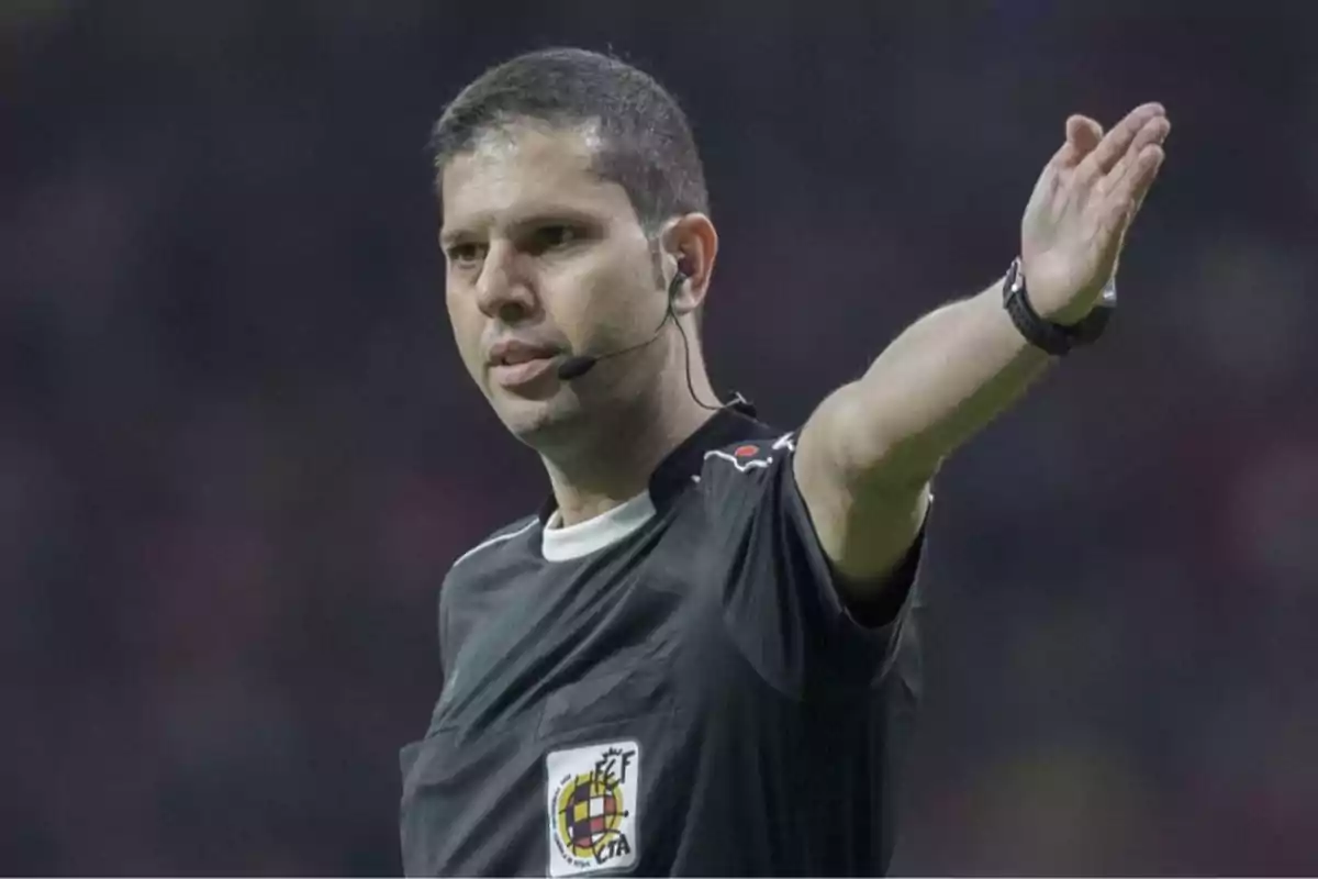 Soccer referee signaling a play during a match while wearing a black uniform and an earpiece
