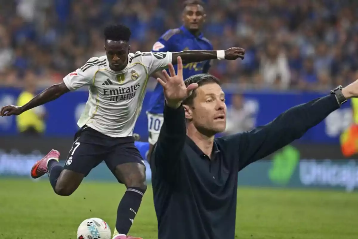 Un jugador del Real Madrid patea el balón durante un partido mientras un entrenador da indicaciones con los brazos extendidos en la banda