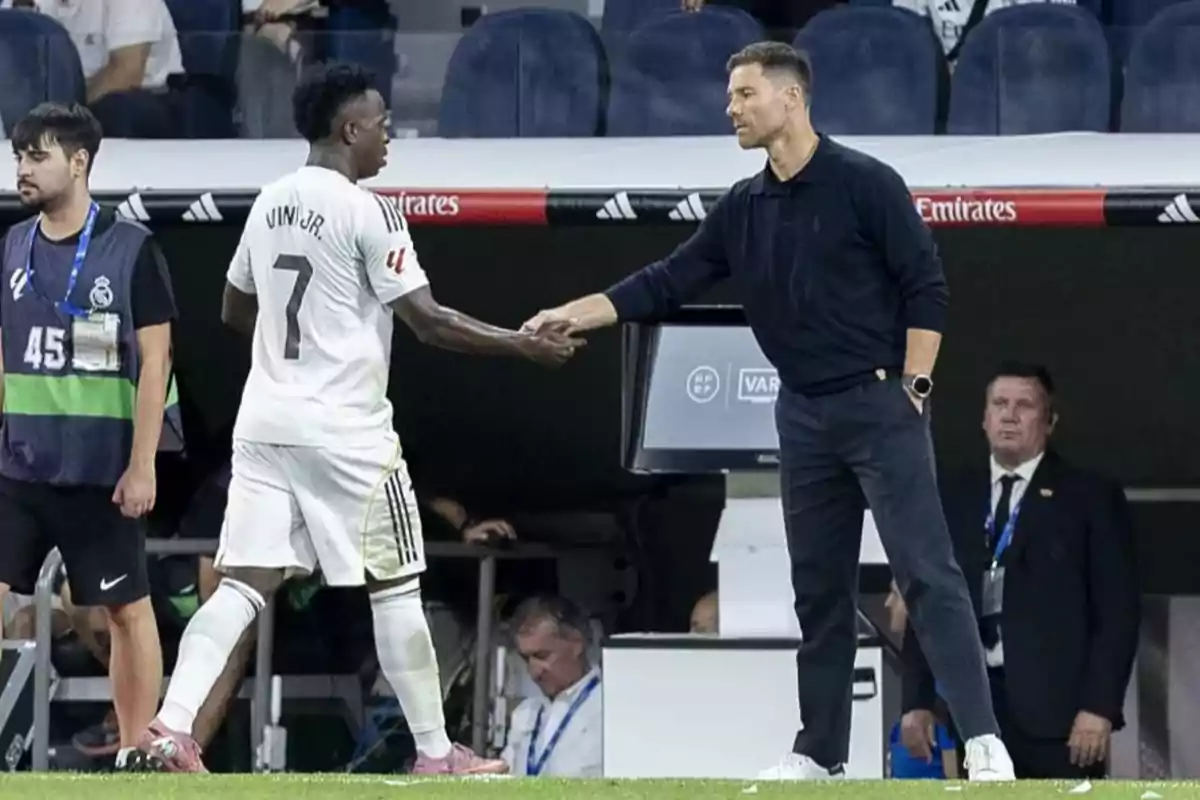 A player wearing Real Madrid’s white uniform shakes hands with a coach in the technical area of the stadium during a match. A player wearing Real Madrid’s white uniform shakes hands with a coach in the technical area of the stadium during a match.
