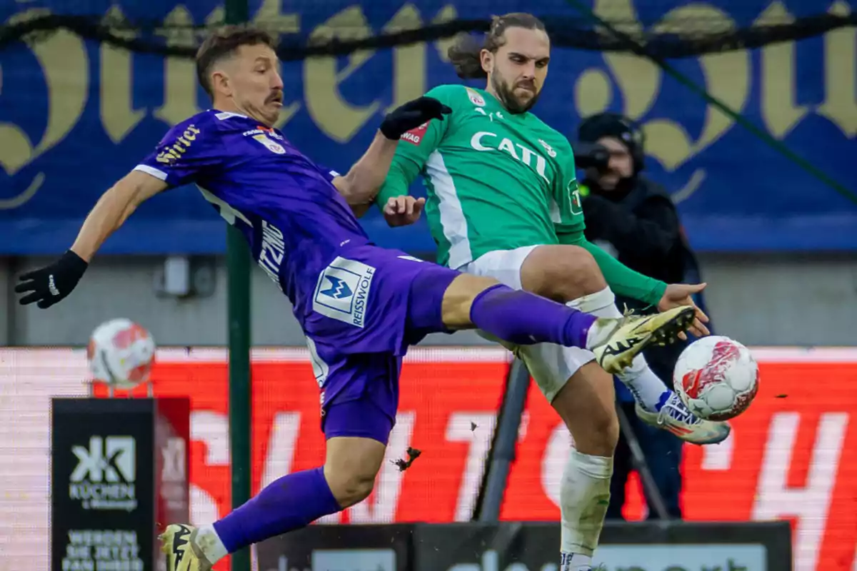 Two players compete for the ball in a match, one dressed in purple and the other in green, both raising their legs to try to control the ball. Two players compete for the ball in a match, one dressed in purple and the other in green, both raising their legs to try to control the ball.
