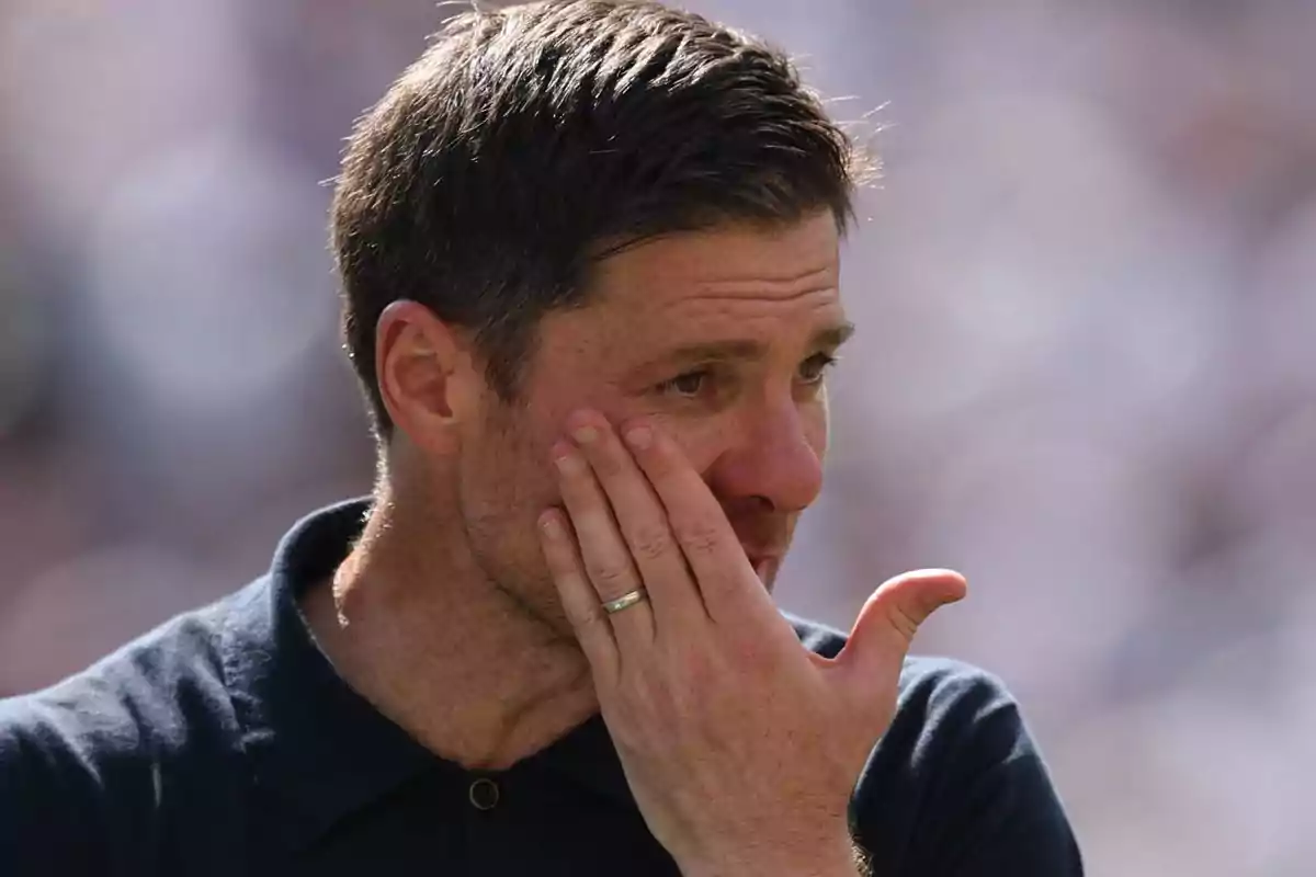 Man with a sad expression covers part of his face with his hand in an outdoor setting.