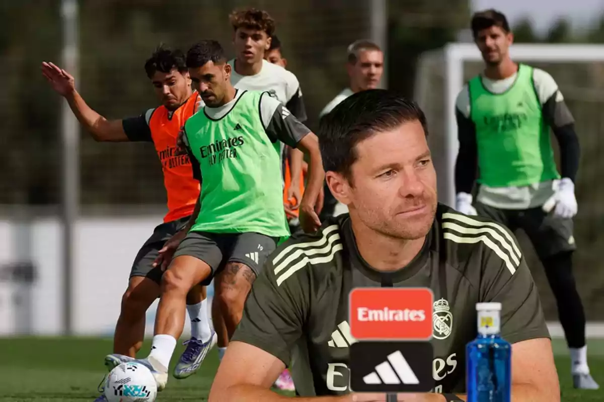 Real Madrid soccer coach at a press conference with players training on the field in the background