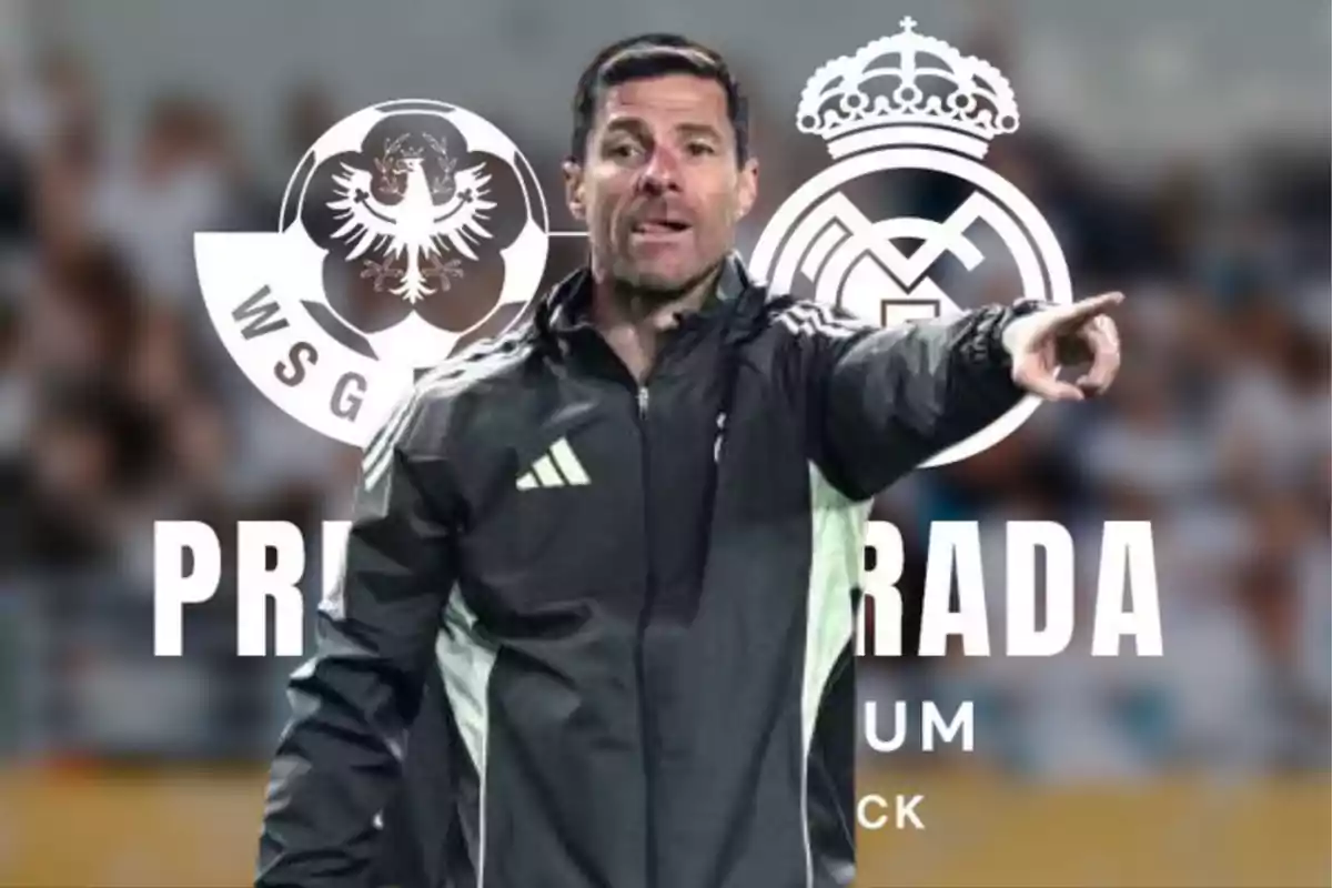 Entrenador de fútbol señalando con el brazo extendido, al fondo se ven los escudos de dos equipos y público desenfocado