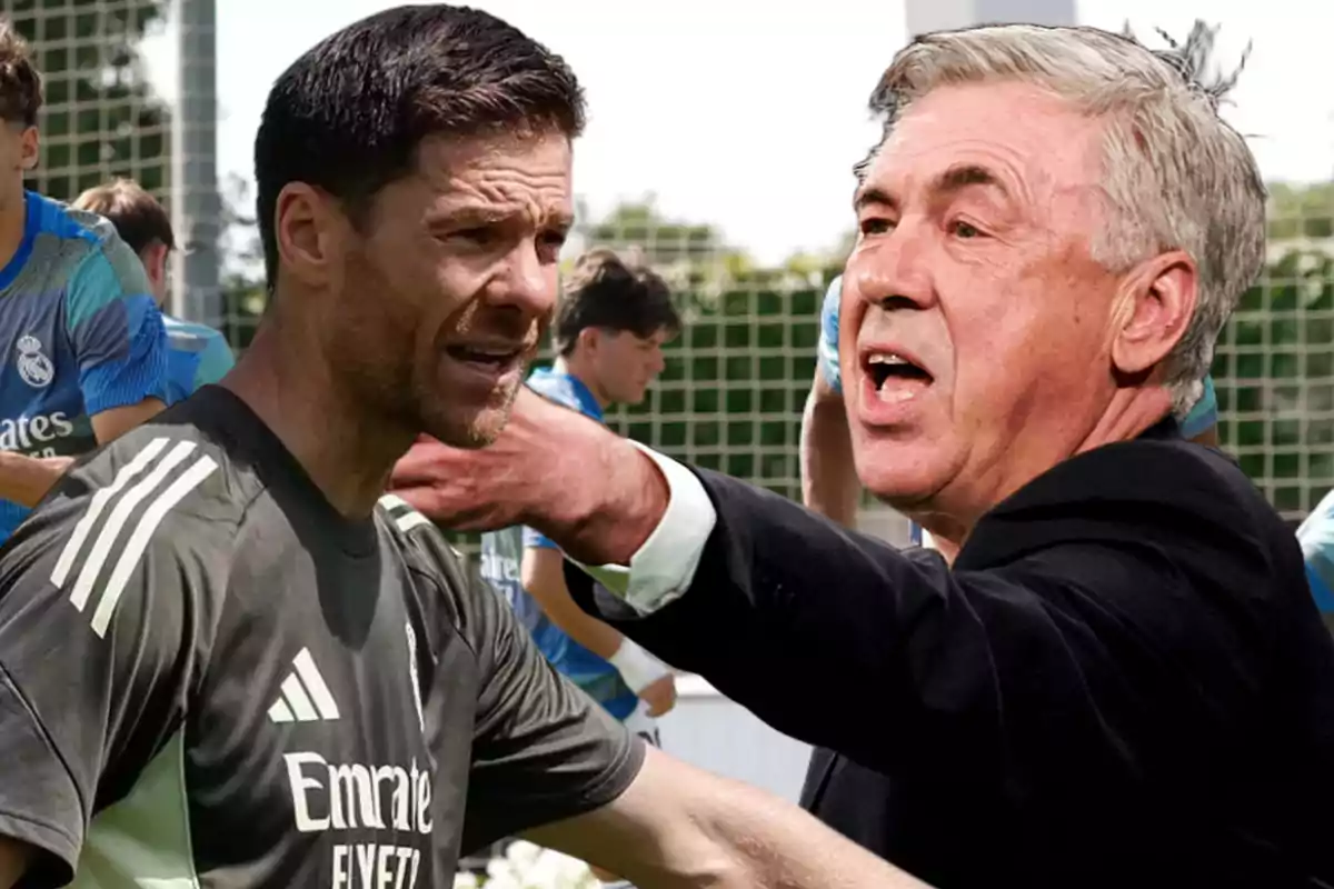Dos entrenadores de fútbol del Real Madrid aparecen en primer plano durante un entrenamiento, uno de ellos parece estar dando indicaciones mientras el otro escucha atentamente, al fondo se ven jugadores con uniforme de entrenamiento.