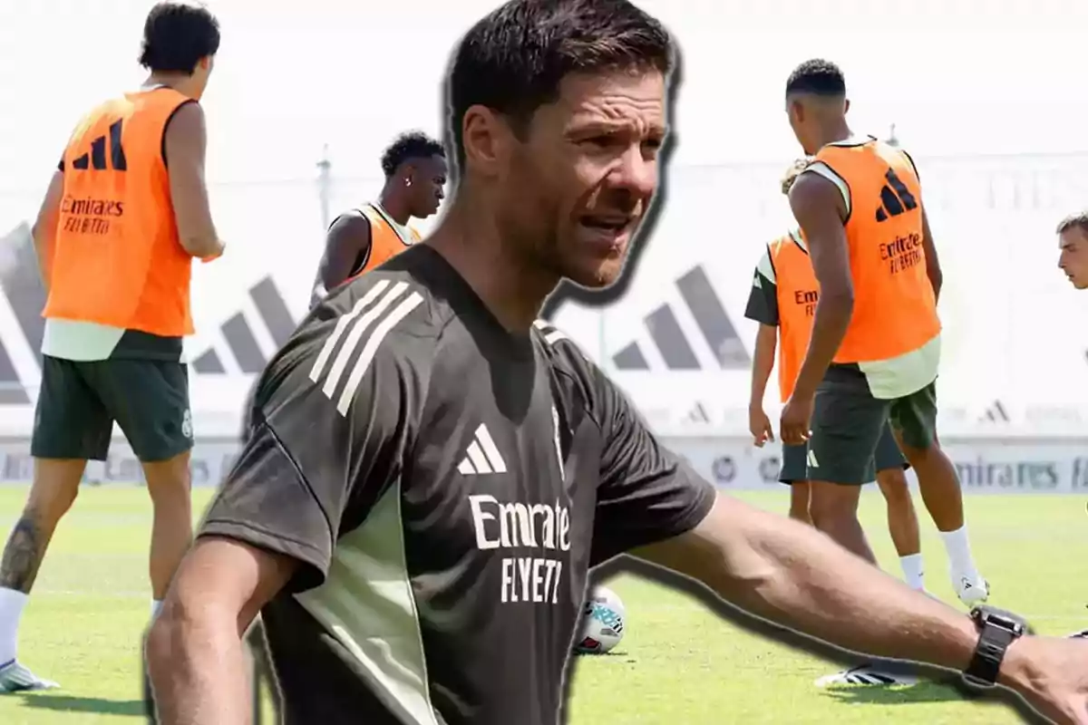 Soccer coach giving instructions on a training field while several players practice wearing orange vests.