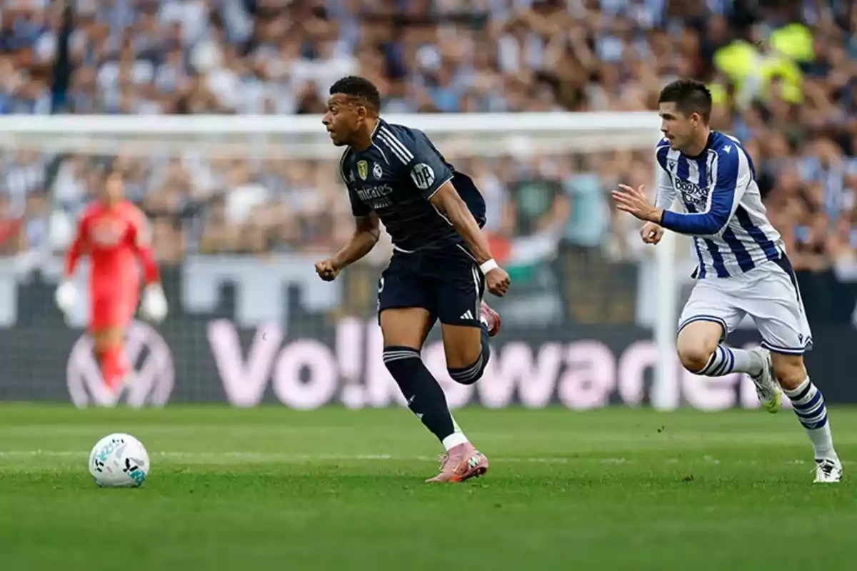 Two players compete for the ball during a match while a goalkeeper watches from the background. Two players compete for the ball during a match while a goalkeeper watches from the background.