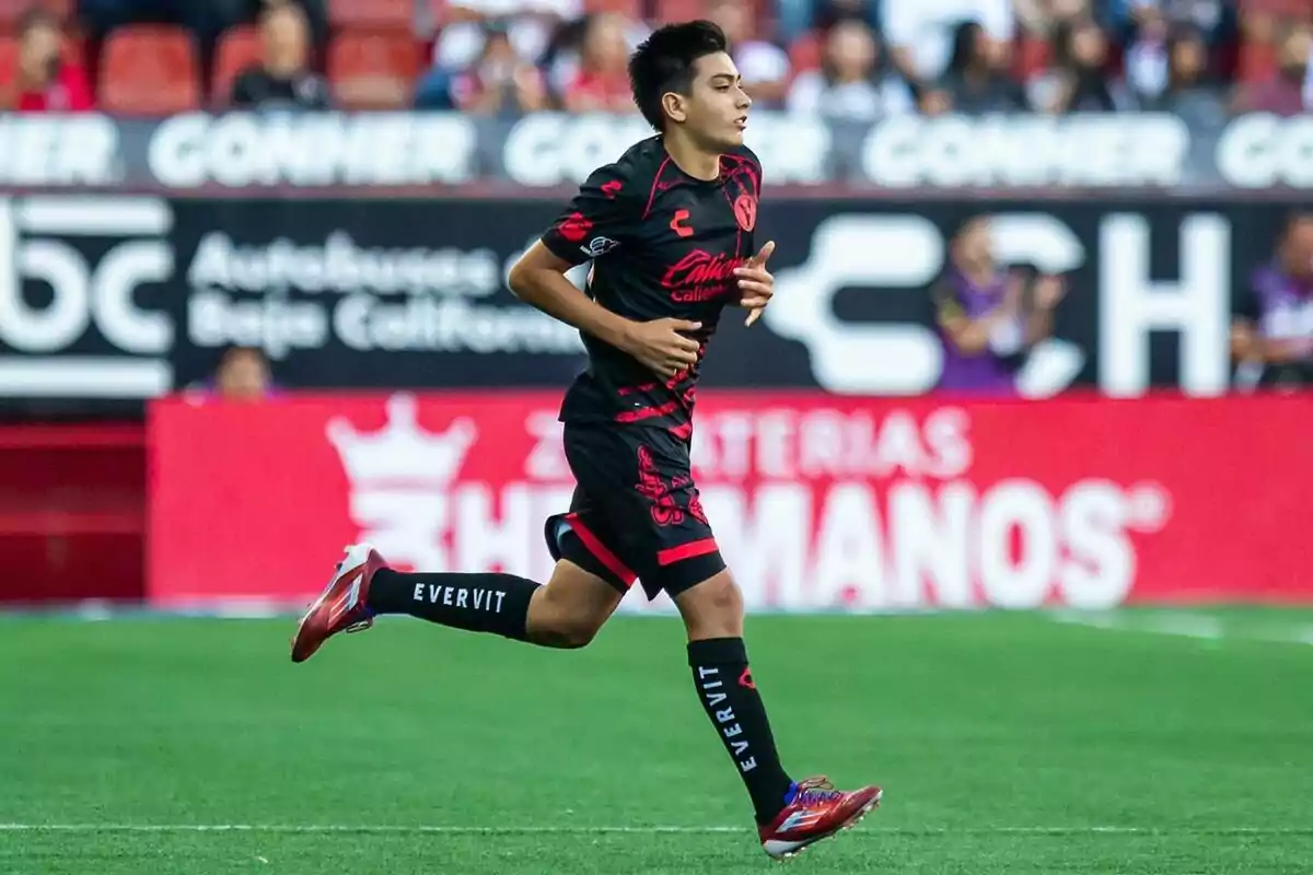 Young player running on the field during a match wearing a black and red uniform Young player running on the field during a match wearing a black and red uniform