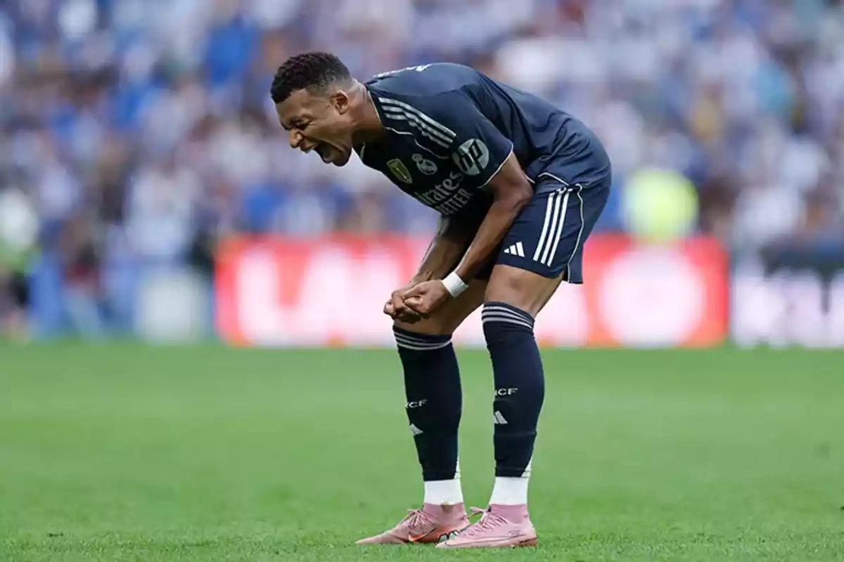 Soccer player in a navy blue uniform screams in pain on the field during a match