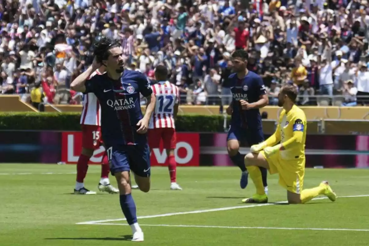 Futbolista celebra un gol en un partido mientras el portero rival permanece de rodillas y la afición llena las gradas del estadio Futbolista celebra un gol en un partido mientras el portero rival permanece de rodillas y la afición llena las gradas del estadio