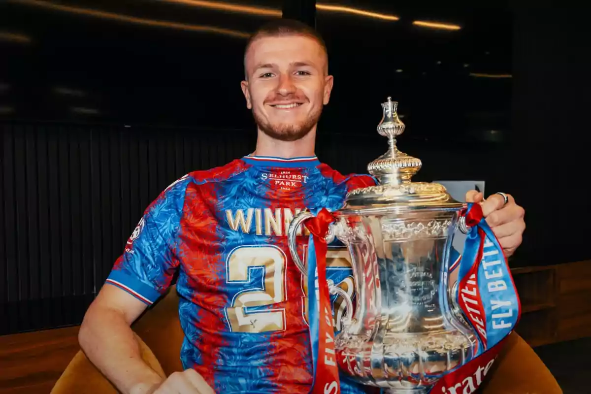 Smiling player in a blue and red jersey holds a silver trophy with red and blue ribbons Smiling player in a blue and red jersey holds a silver trophy with red and blue ribbons